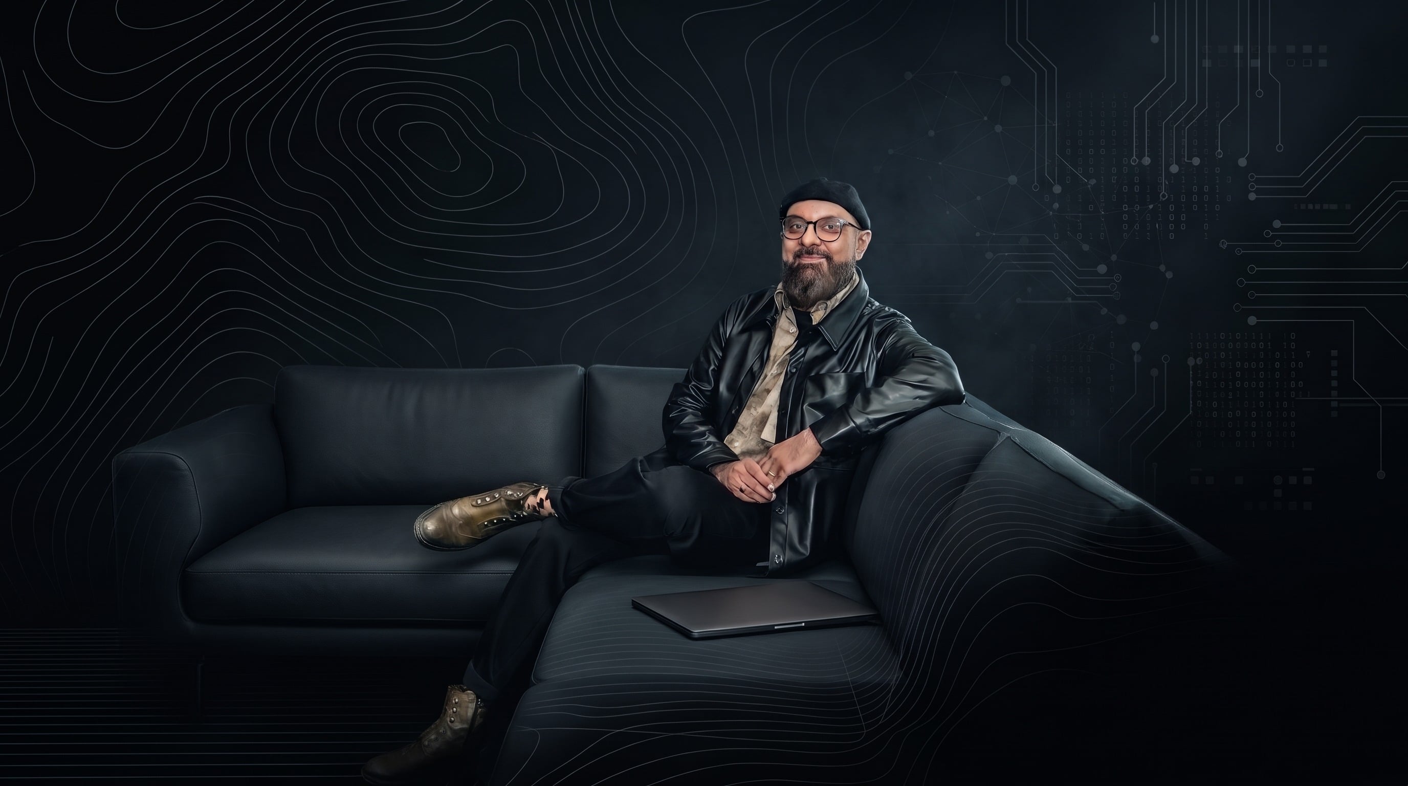 Mansur Mirani seated on a black leather sofa, with contour lines and circuit traces behind him