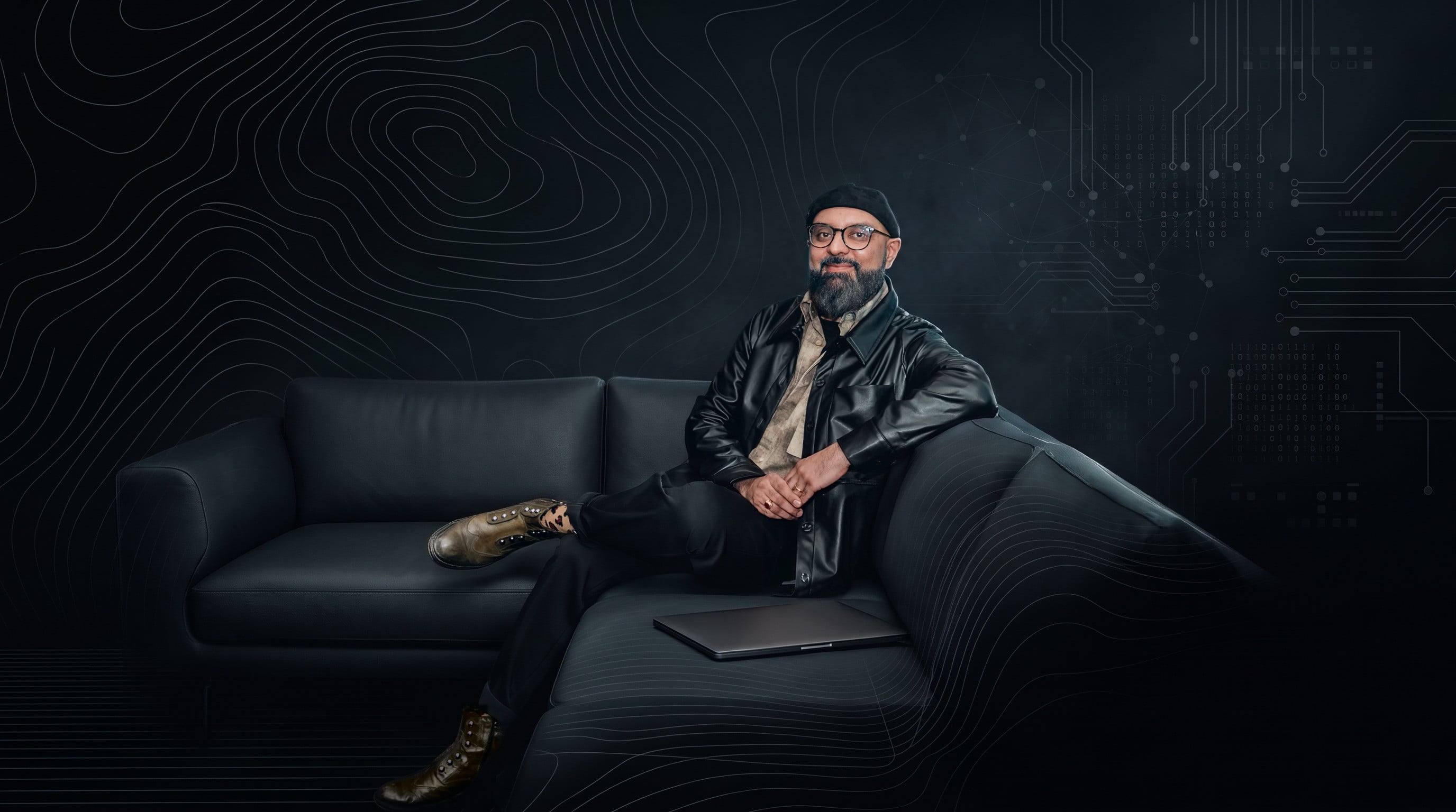 Mansur Mirani seated on a black leather sofa, with contour lines and circuit traces behind him